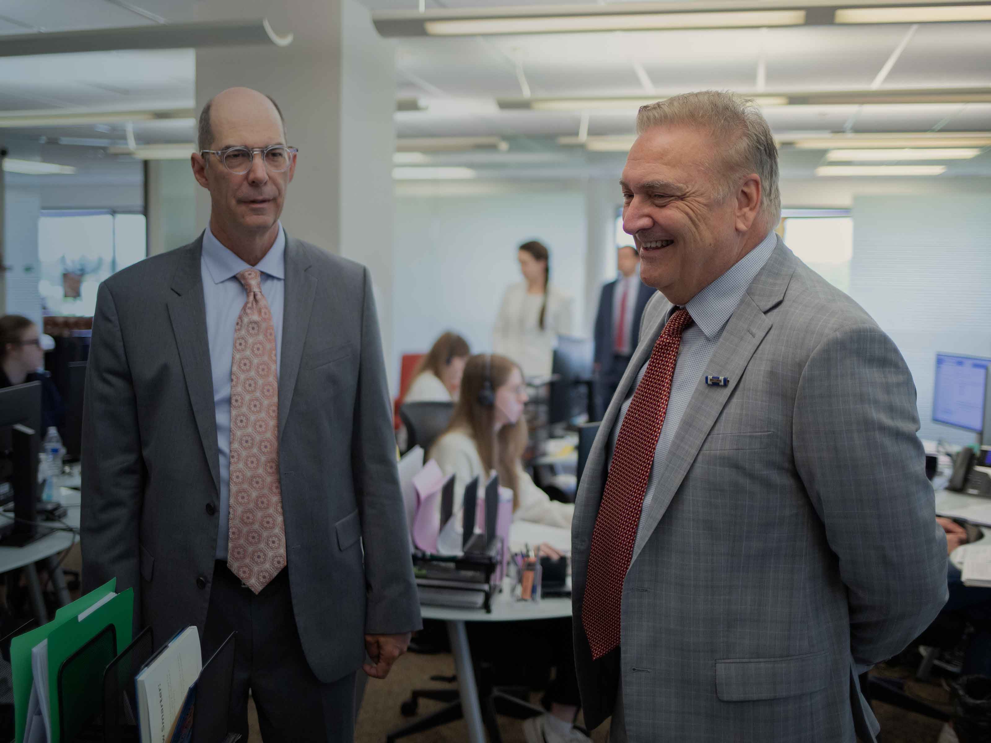 Two BIRG Law attorneys talking in the open-plan office while the team works at their desks behind them