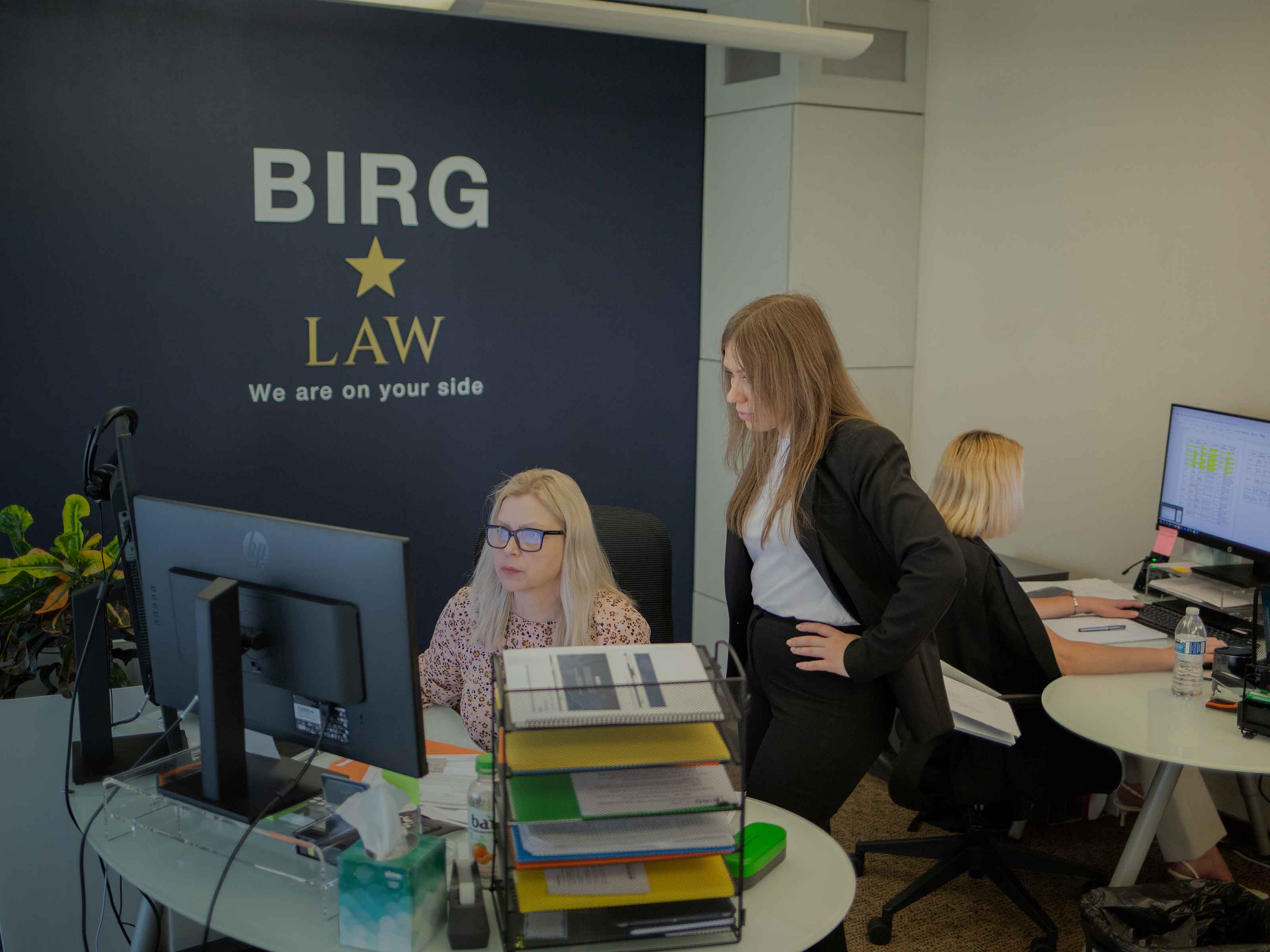 BIRG Law team members working at their desks beside the We are on your side branded wall