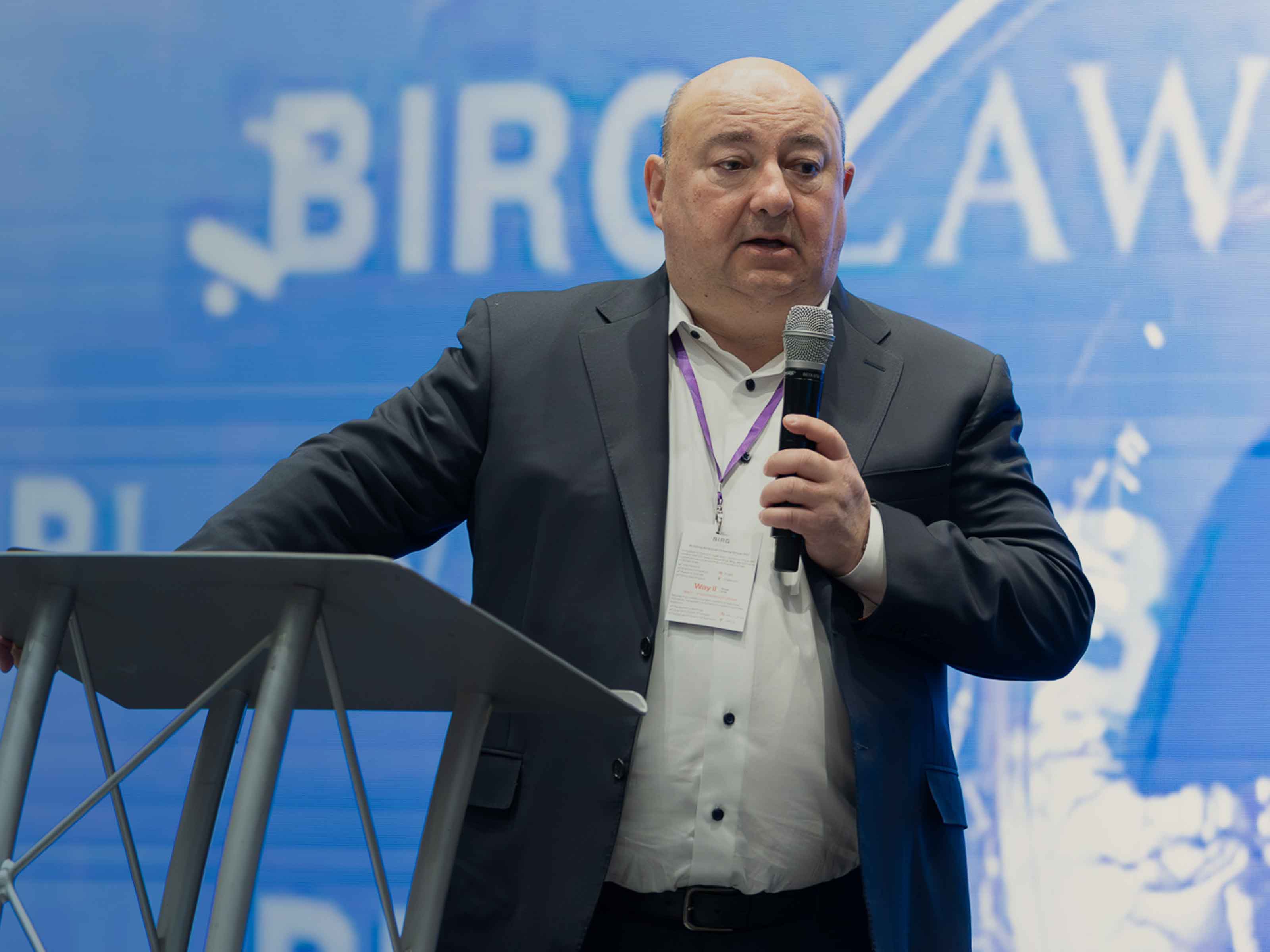 Yuri Birg speaking into a microphone at a lectern in front of a BIRG Law event backdrop
