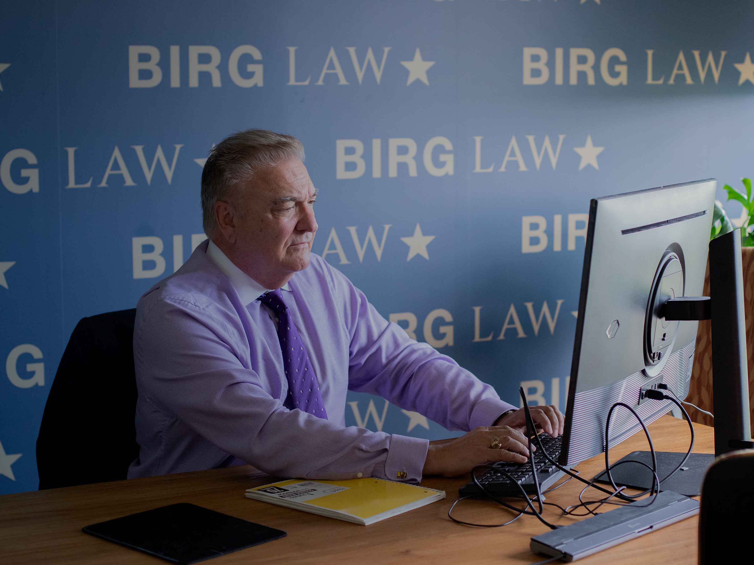 A BIRG Law attorney working at his computer in front of the branded BIRG Law wall